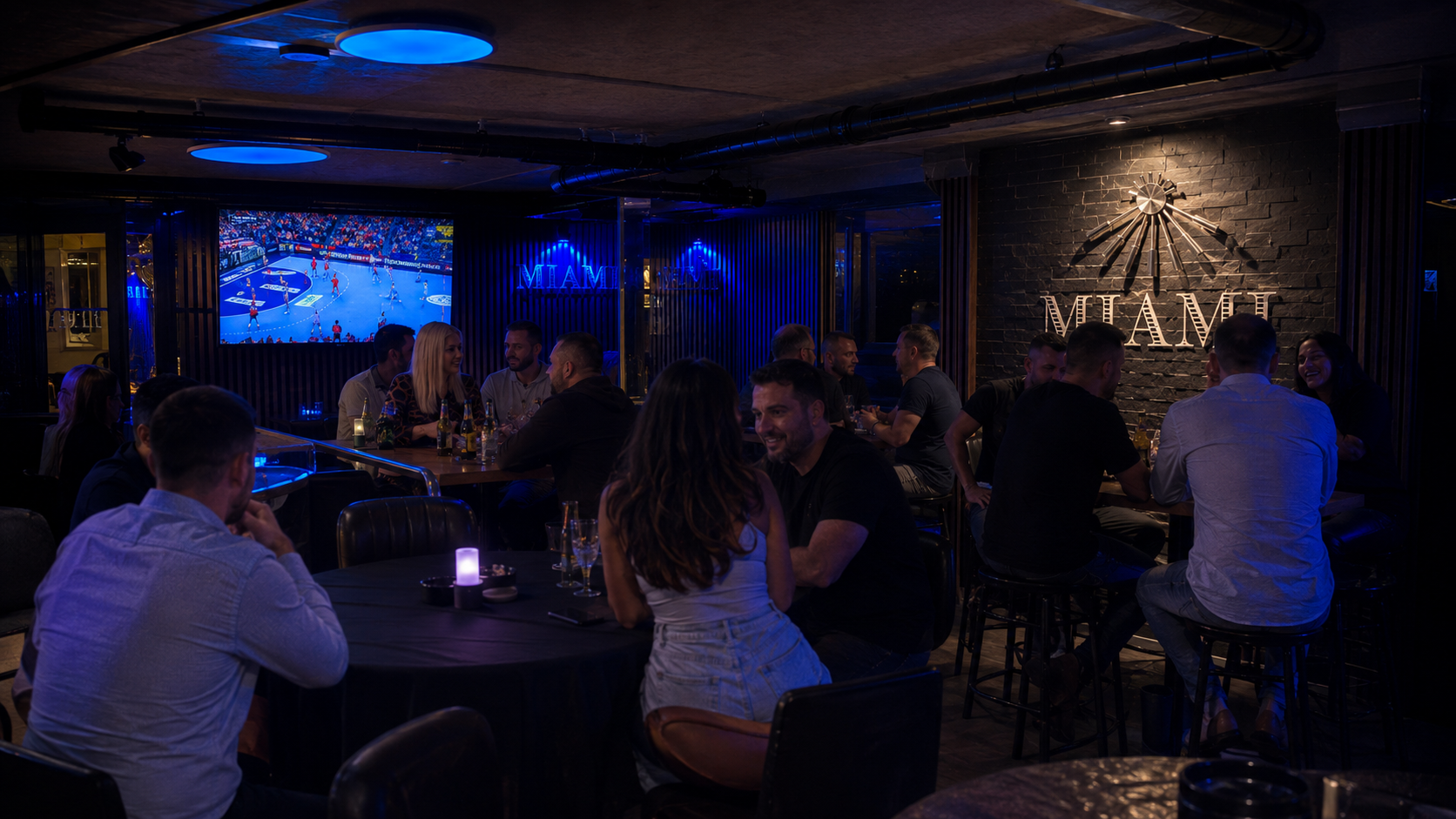 Gäste der Miami Bar sitzen gemeinsam an Tischen vor der beleuchteten MIAMI Wand